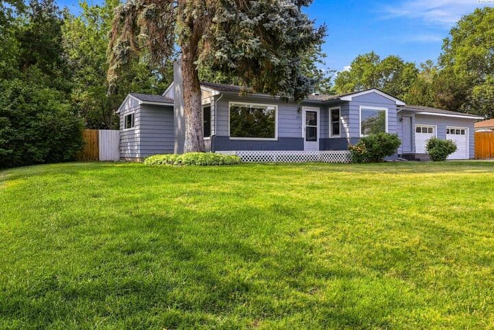 Front of 1613 W 9th Ave in Kennewick — updated single-story home with blue-gray siding, a large evergreen, and a sweeping front lawn